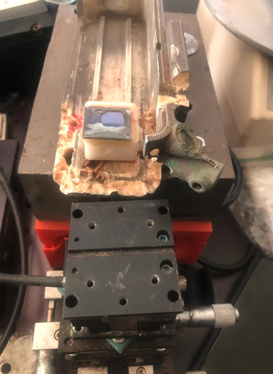 A small chip glued to the end of a thin rail above a black three-axis positioning stage with red printed parts
