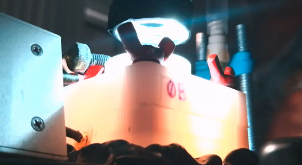 A white plastic block lit from below, with red and blue wing nuts and tubing, beside a metal box