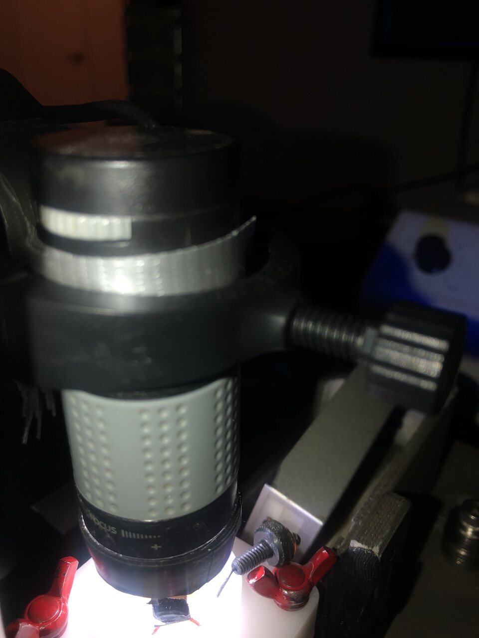 A handheld digital microscope clamped above a white flow cell with red wing nuts